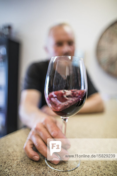 Mann wirbelt während einer Weinprobe ein Glas Rotwein durcheinander.
