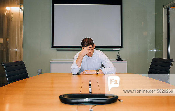 Man sat in a meeting room with his head in his hands looking stressed