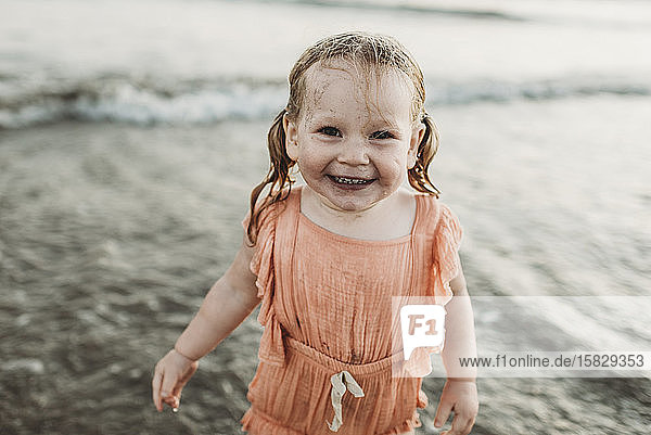 Portrait of toddler girl smiling in ocean at sunset
