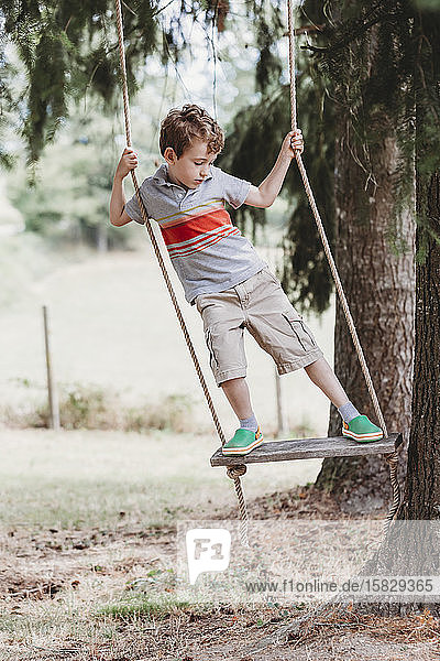 Front view of boy standing on swing  swinging side-to-side under trees