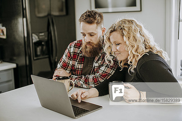 Man and woman couple sit in kitchen with laptop computer and coffee