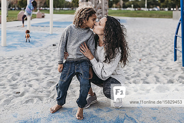Mutter gibt ihrem Sohn einen Kuss  während sie in der Abenddämmerung auf dem Spielplatz spielt