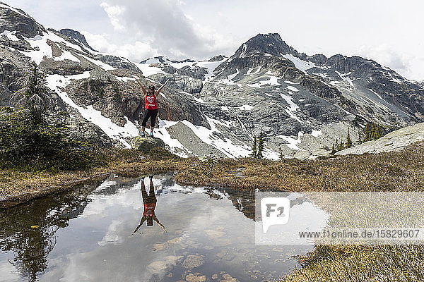 A women stands on a rock and celebrates Canada on a summer day in the mountains of British Columbia.