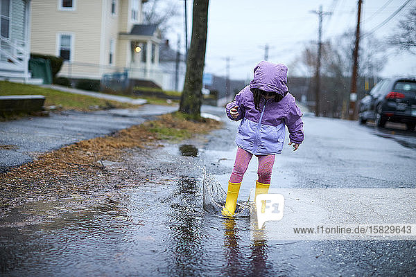 Ein kleines Mädchen  das an einem regnerischen Tag in Pfützen plantschend Spaß hat.