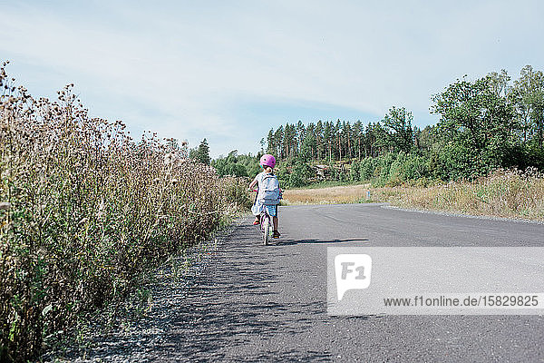 rear view of a young girl cycling home from school along country road