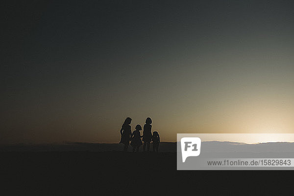 Silhouette of four young sisters at beach during sunset