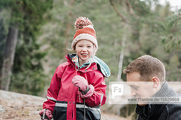 junges Mädchen lächelt und isst einen Marshmallow beim Camping in Schweden