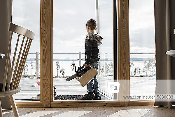 Junge spielt mit Spielzeugwerkzeugen in seinem Haus mit Blick auf das Meer