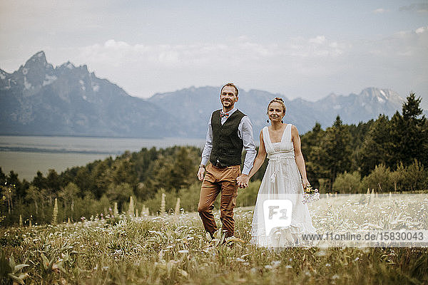 Bride and Groom walk through wildflowers in front of Teton mountains