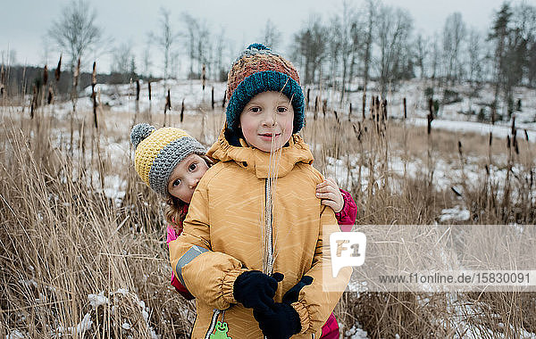 Geschwister spielen  während sie draußen im Schnee in die Kamera schauen