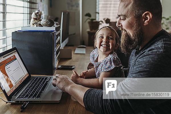 Young preschool aged daughter smiling at dad while he works from home