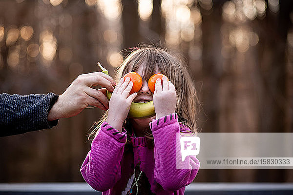 Junges Mädchen legt Obst auf das Gesicht  um draußen ein albernes Gesicht zu machen