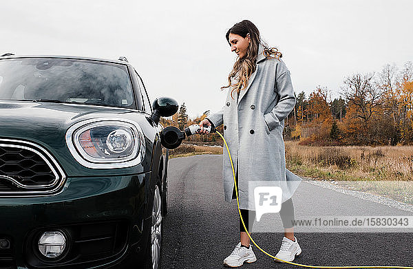 Frau  die ihr Elektroauto auf einer Landstraße in Schweden einsteckt