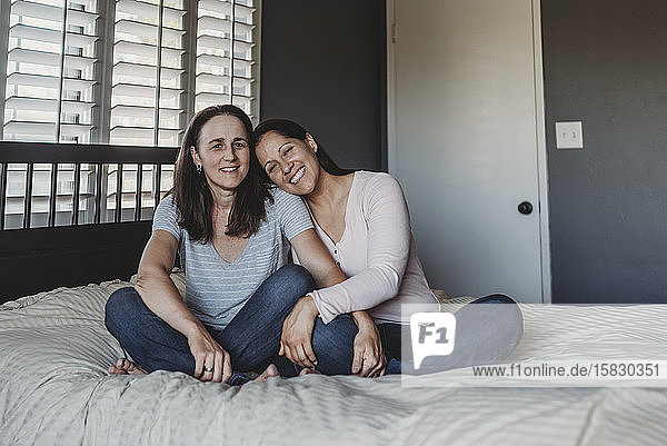 Happy same sex spouses sitting on bed snuggling
