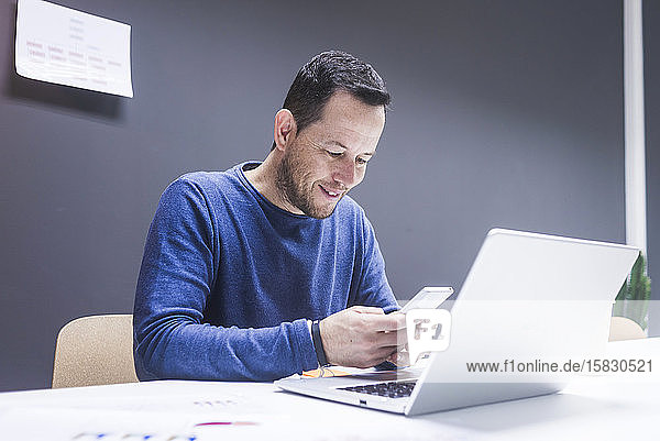 Young businessman reading his smartphone. Portrait of business man reading message with smartphone in office. Man working at his desk at office.