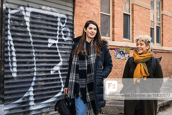 Friends talking while walking together by building in city during winter