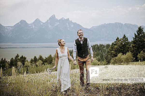 Newlywed bride and groom walk through field in Grand Teton Park.