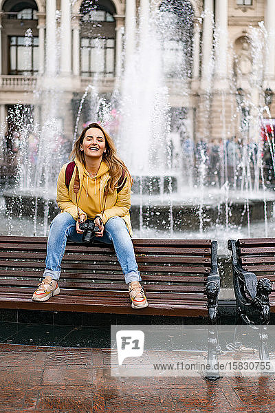 Junge Touristin mit einer Kamera lacht auf Bank in der europäischen Altstadt