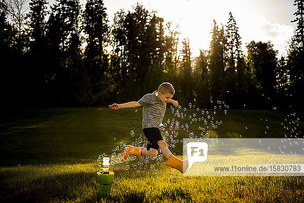5 year old boy jumping through bubbles in golden light