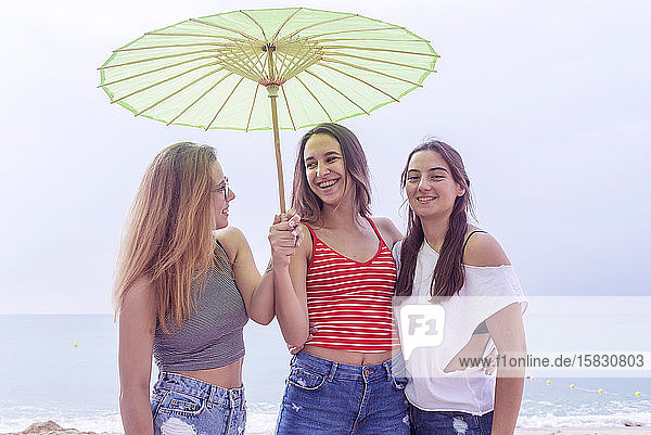 Glückliche junge Frauen haben Spaß am Strand unter einem Sonnenschirm