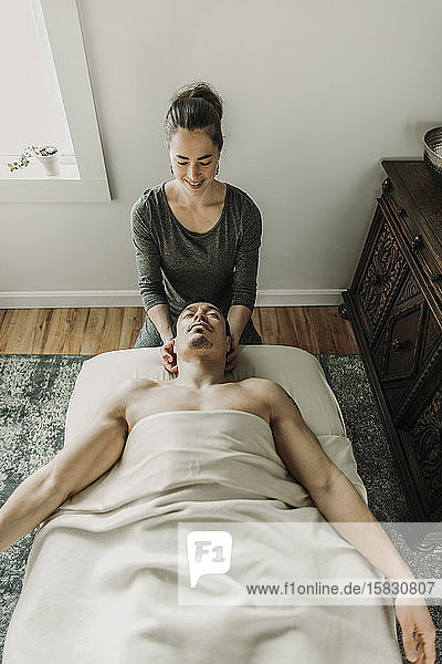 Lächelnde weibliche Massagetherapeutin behandelt Nacken des männlichen Patienten