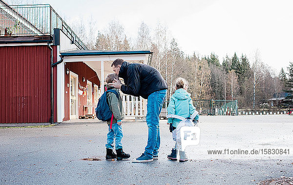 father kissing his kids goodbye at the school gates