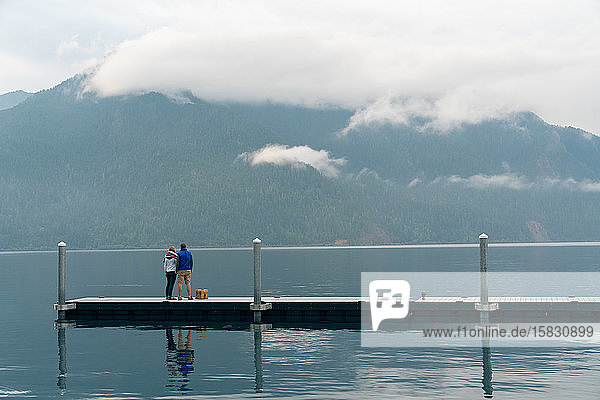 Man and woman standing on dock looking at foggy mountans