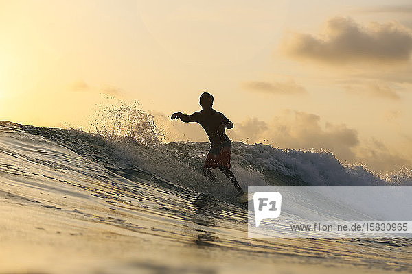 Junger Mann surft bei Sonnenuntergang