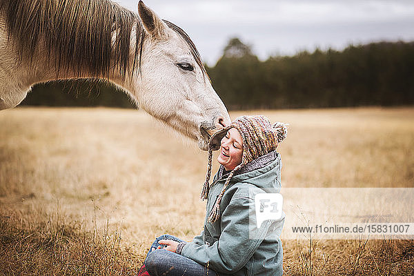 white horse playing with young girls hat while sitting in field