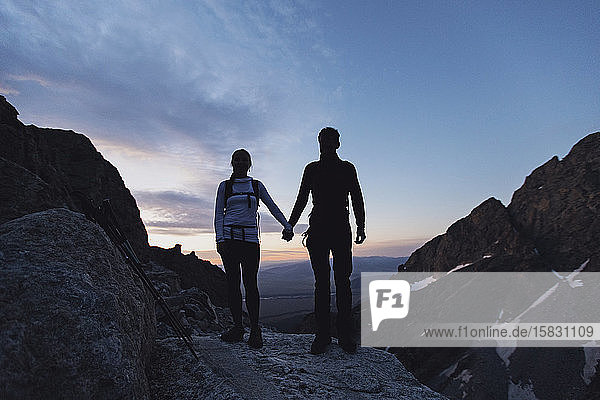 Couple holds hands while hiking at sunrise in the mountains