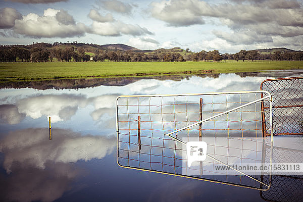 Dramatische Spiegelung des Sees mit Wolken und Zaun überschwemmtes Tor auf dem Bauernhof