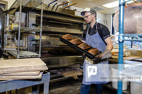 Ein professioneller Bäcker trägt ein Tablett mit frisch gebackenem Brot aus dem Ofen