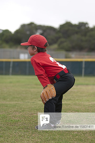 Young boy with his hands and glove on his kees on a baseball field