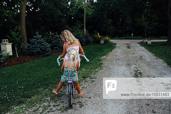 Zwei Mädchen fahren im Sommer mit dem Fahrrad eine Einfahrt hinunter