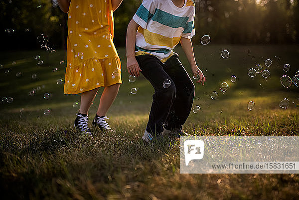 Geschwister springen in Seifenblasen in goldenem Licht gesichtslos