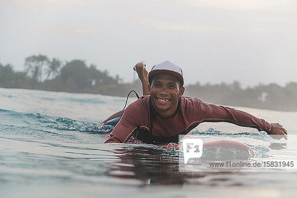 Porträt eines glücklichen Mannes, der auf einem Surfbrett auf dem Meer liegt