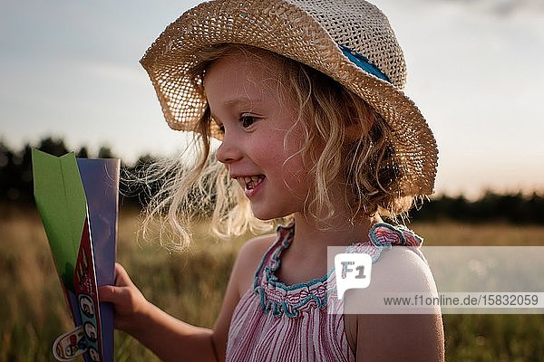 Nahaufnahme des Porträts eines jungen Mädchens  das bei Sonnenuntergang mit Papierflugzeugen spielt