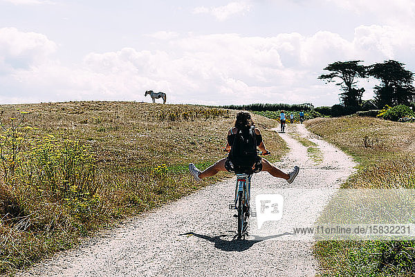 Hübsche junge Frau fährt Fahrrad mit offenen Beinen auf einer Landstraße