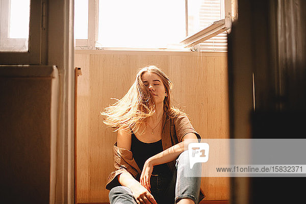 Teenager-Mädchen  das im Sommer auf dem Balkon auf dem Boden sitzend mit den Haaren wackelt