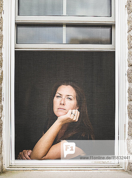 Woman looking out of open window with chin resting on hand.