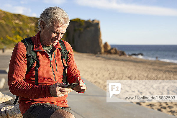 Älterer Mann benutzt Smartphone  während er am Strand steht