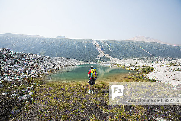 Rückansicht des Rucksacktouristen mit Blick auf den alpinen Bergsee.