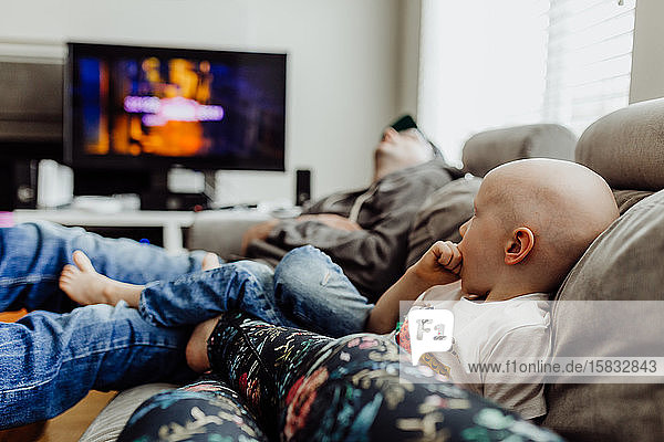 Familie entspannt sich auf der Couch und sieht fern  während Papa ein Nickerchen macht