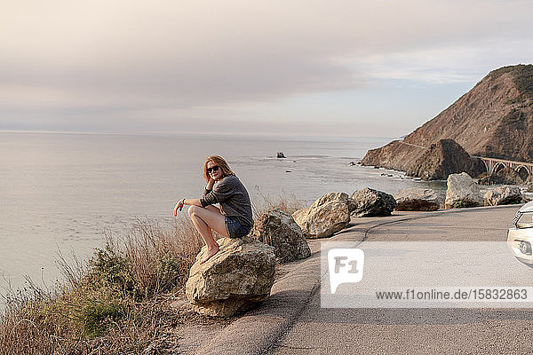 Frau sitzt auf einem Felsen am Aussichtspunkt Big Sur