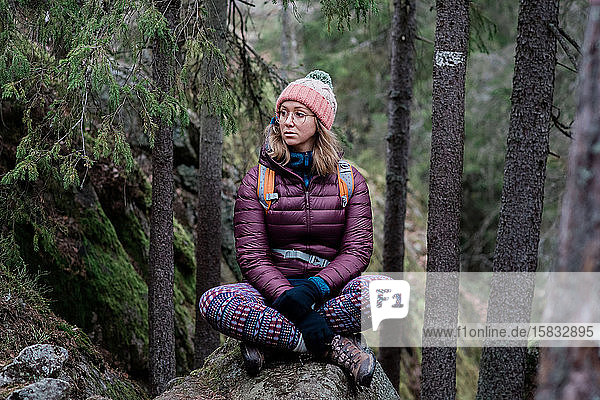 Frau sitzt auf einem Felsen und denkt beim Wandern im Wald in Schweden nach