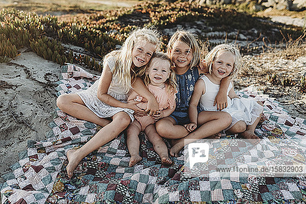 Vier Schwestern sitzen am Strand auf einer Decke und lächeln bei Sonnenuntergang