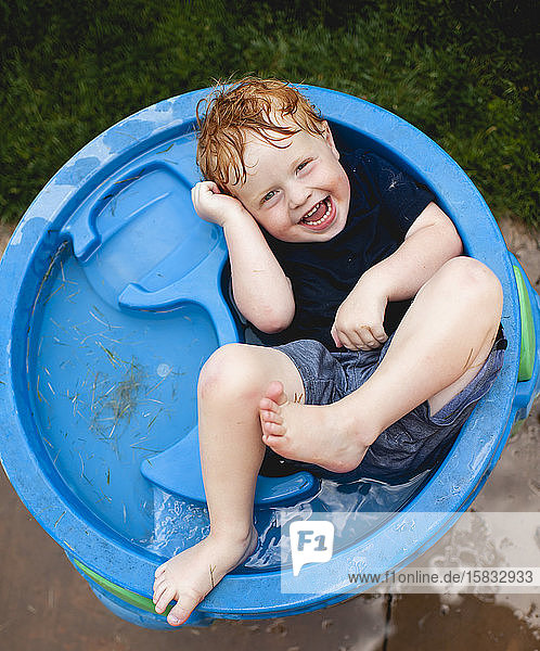 Kleinkind liegt mit Kleidung auf dem Grundwasserspiegel und lacht im Garten