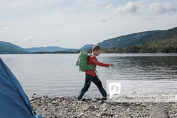 young boy hiking with backpack whilst camping by the mountains