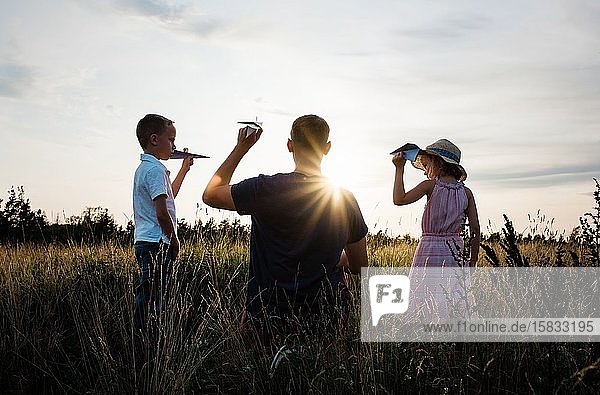 Vater spielt mit seinem Sohn und seiner Tochter bei Sonnenuntergang auf einer Wiese
