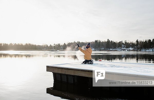 Junge wirft Schnee in die Luft  während er draußen an der Ostsee spielt